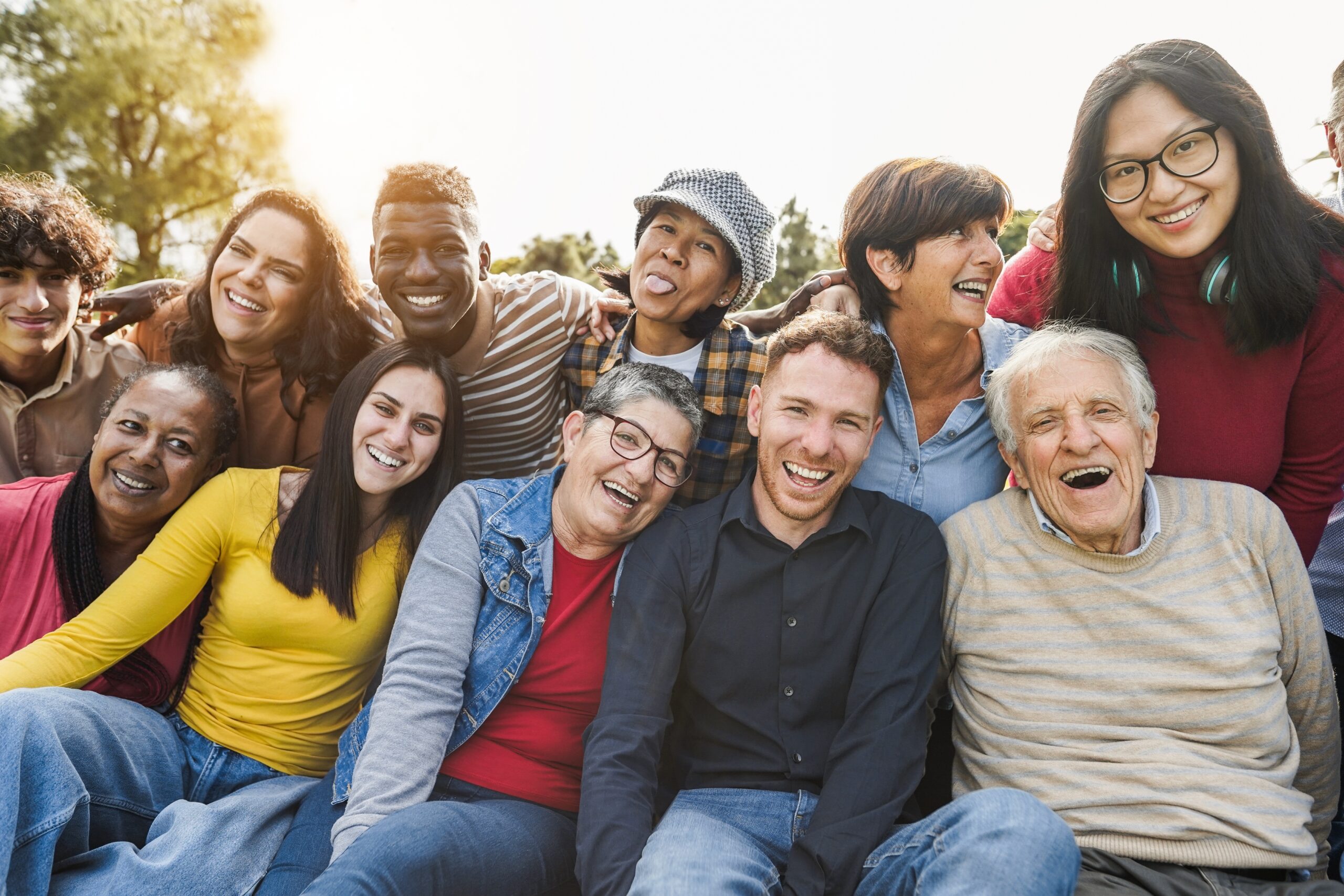 A joyful, diverse group of people of different ages and backgrounds gathered closely, smiling and laughing together.
