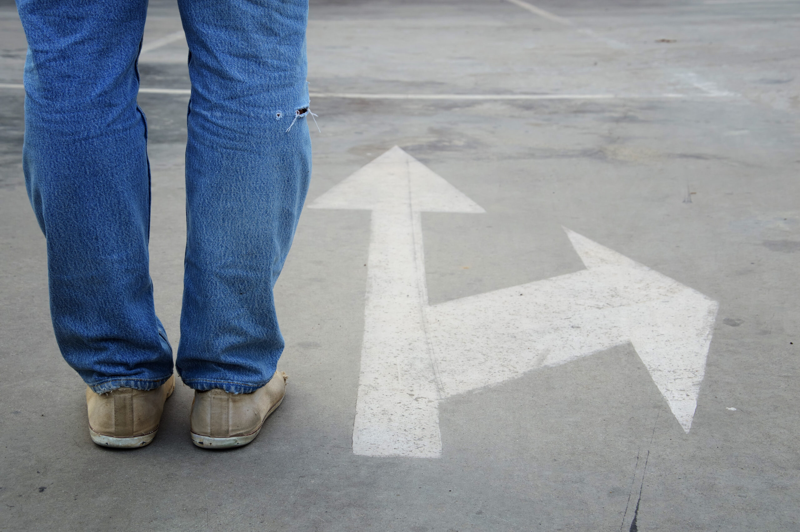 A person standing at a fork in the road with arrows pointing in two directions, symbolizing life's unexpected detours and choices.