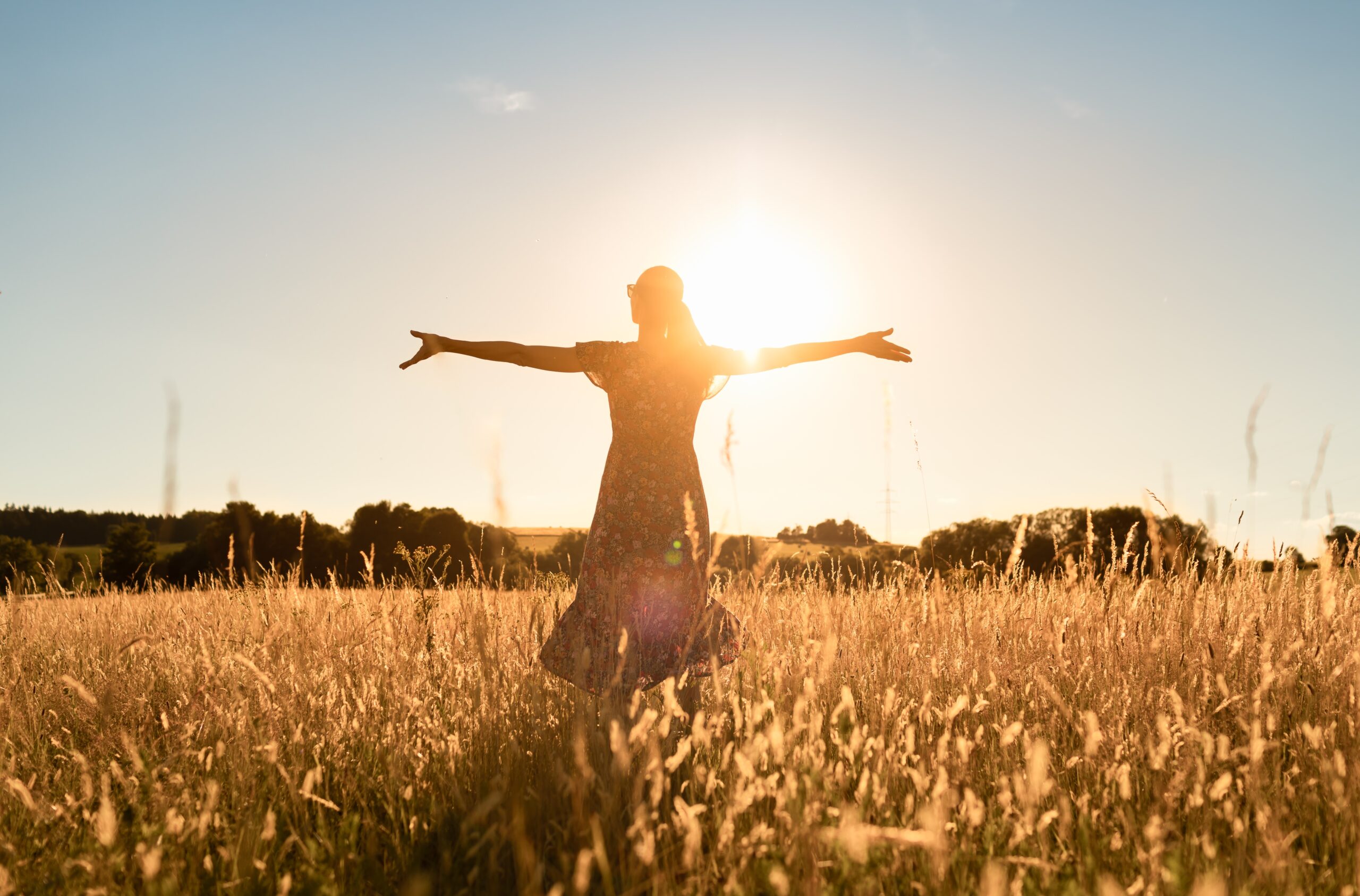 A woman standing in a sunlit field with arms wide open, symbolizing freedom, acceptance, and the beauty of letting go.