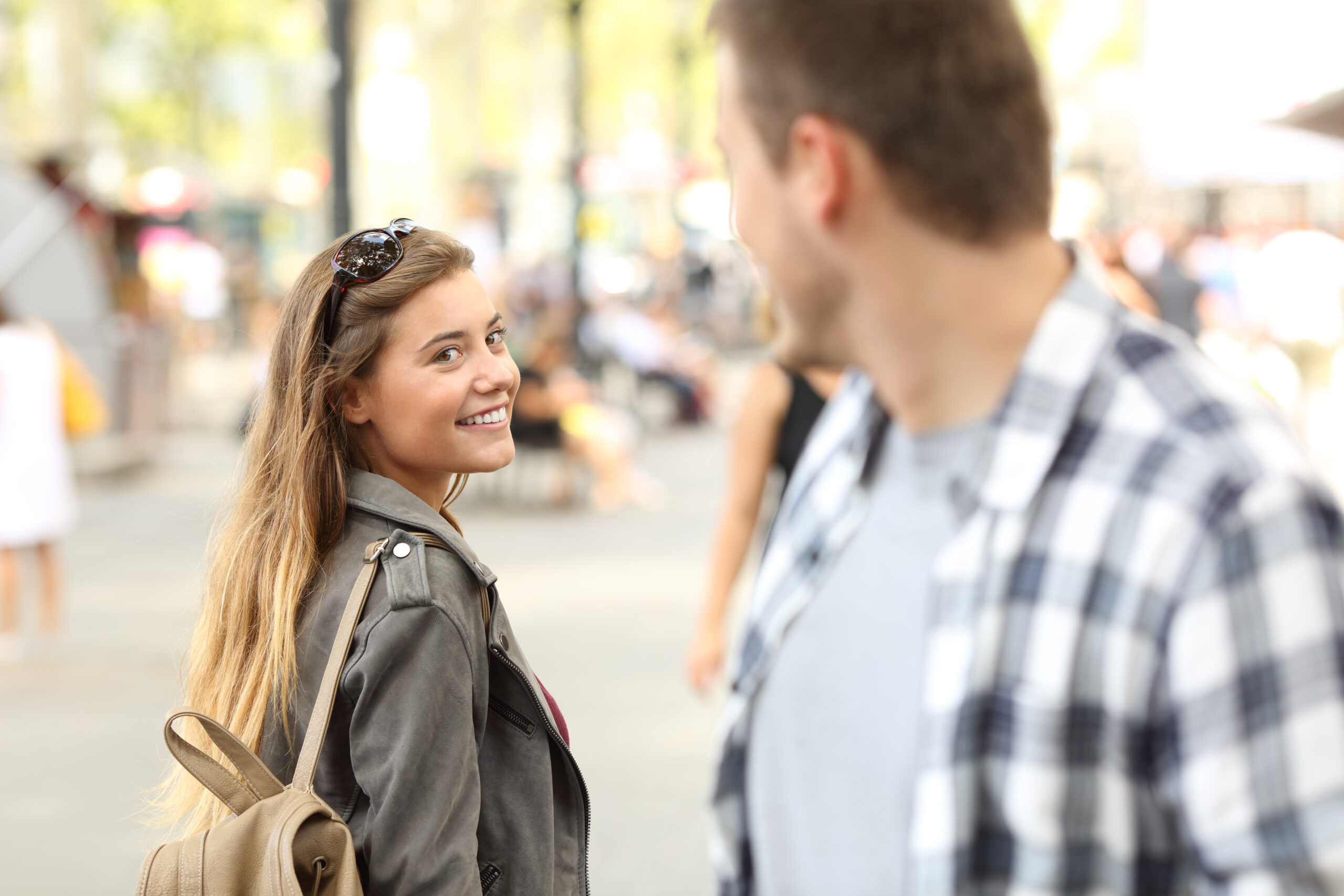 A smiling young woman glances back during a brief encounter on a busy street, capturing the unexpected impact of small moments.