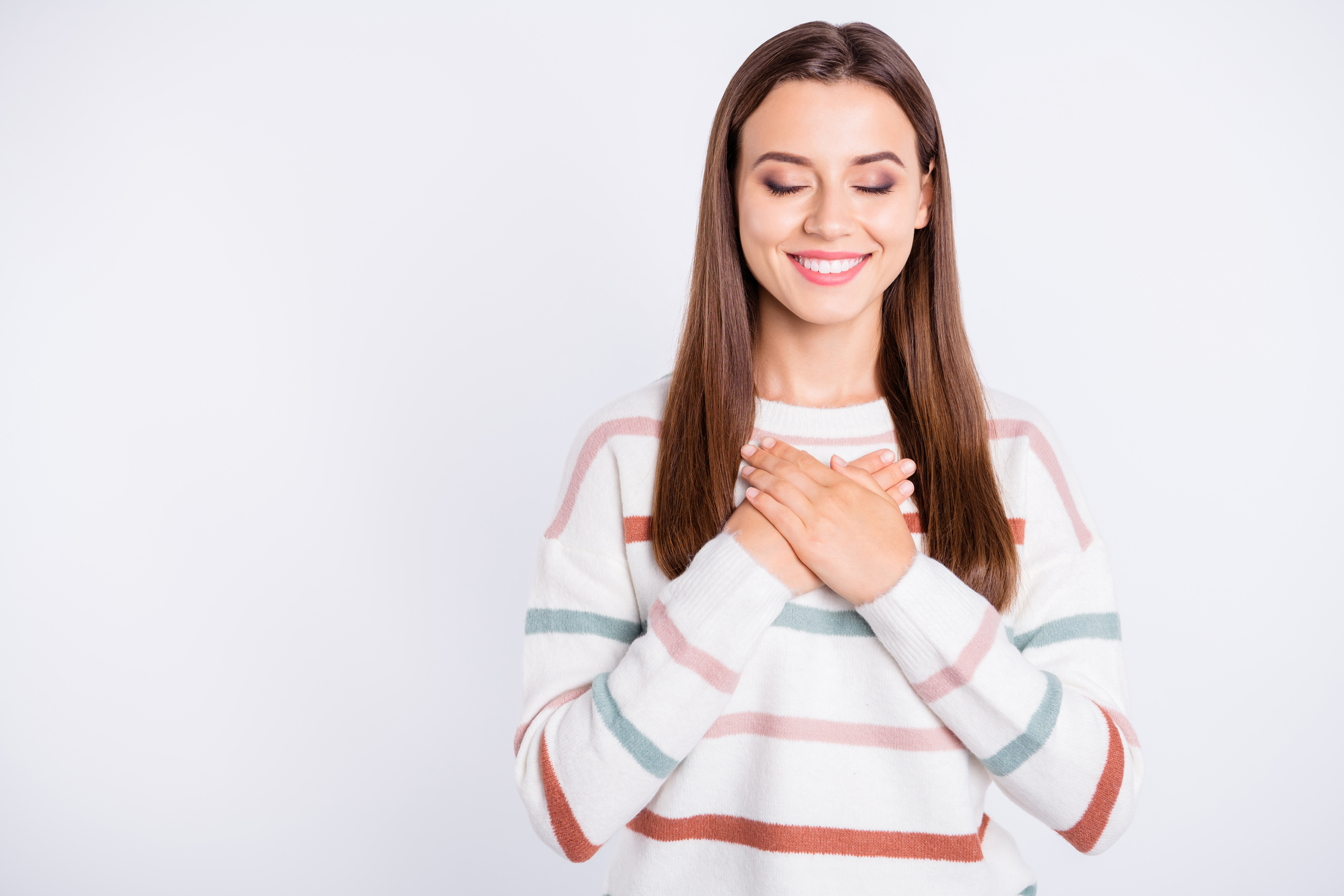 A woman with her hands over her heart and eyes closed, smiling peacefully, representing self-trust and inner confidence in moments of doubt.