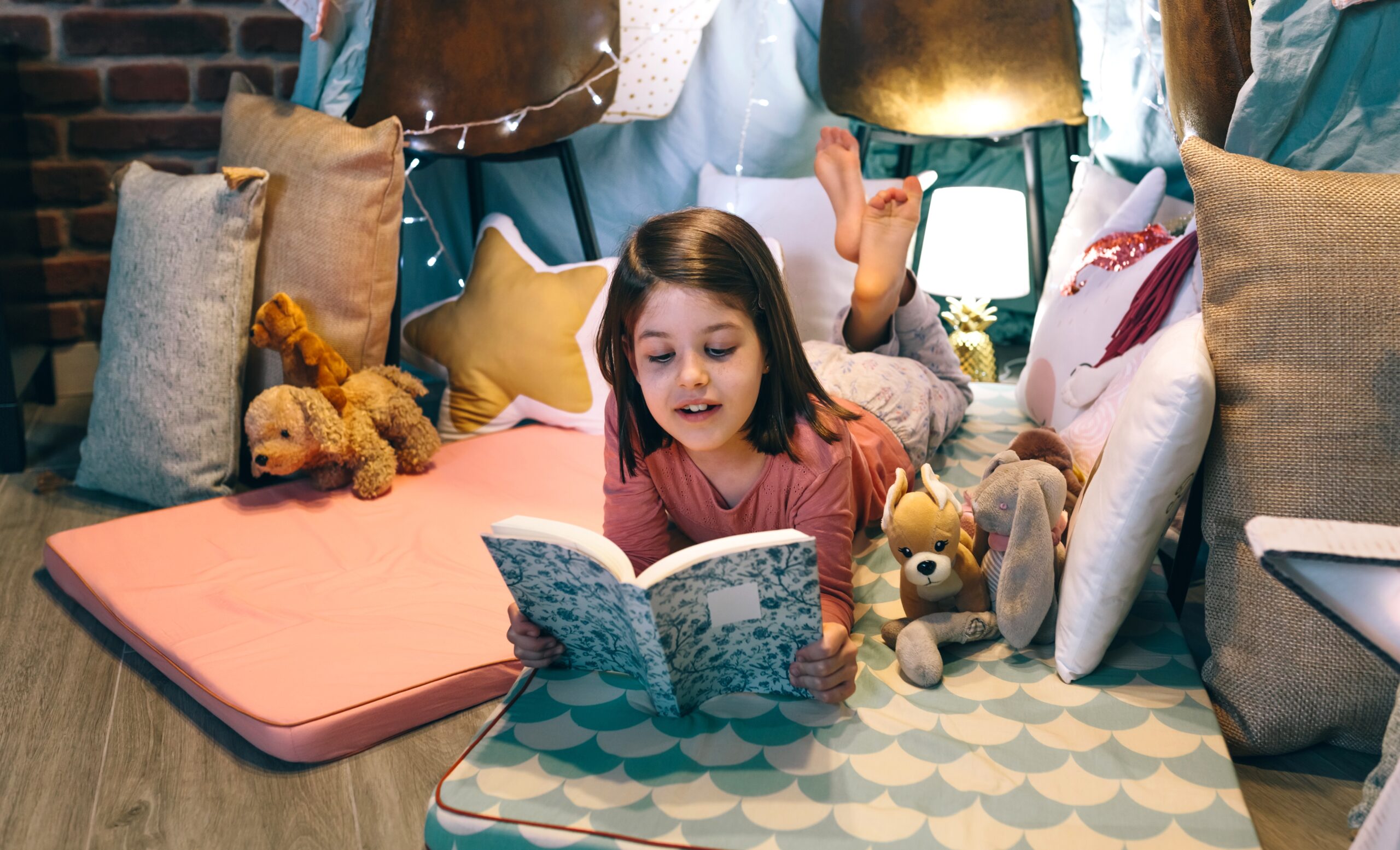 A young girl reading a fairy tale book in a cozy pillow fort, surrounded by soft toys and magical lights—lost in the wonder of storytelling.