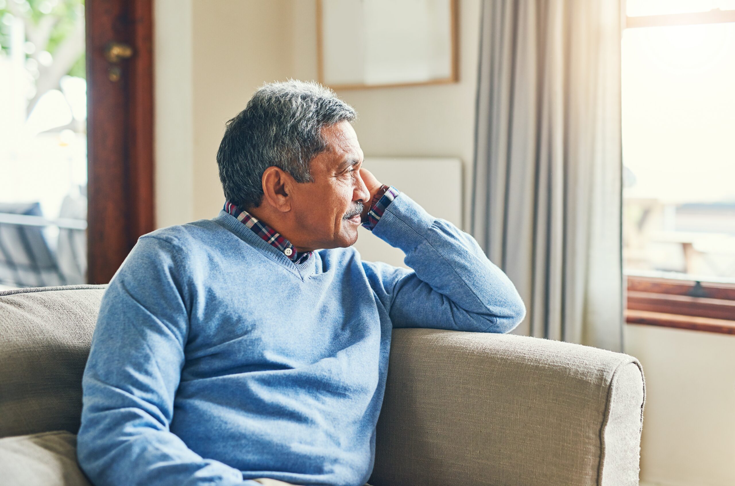 An older man sitting on a couch, gazing out the window with a thoughtful expression—reflecting on life’s meaningful mistakes.
