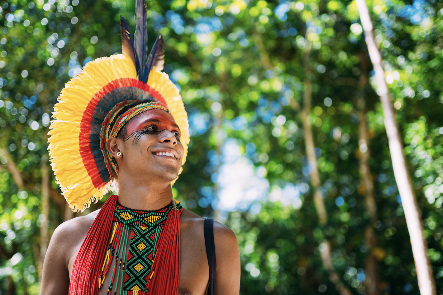 An Indigenous person in traditional attire, smiling under the forest canopy—embodying deep-rooted wisdom about living in harmony with nature.