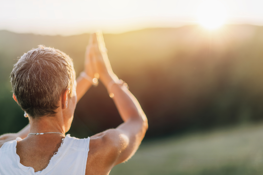 A person facing the sunrise with hands in a prayer position, symbolizing morning rituals that connect mind and intuition.